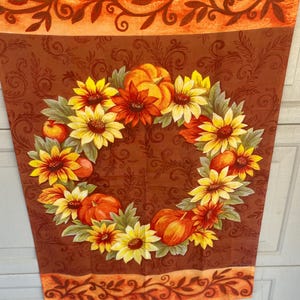 May include: A fall-themed decorative banner featuring a wreath of sunflowers, pumpkins, and apples. The banner has a brown background with a floral pattern and an orange border with leaf designs. The color palette includes shades of orange, yellow, and brown.