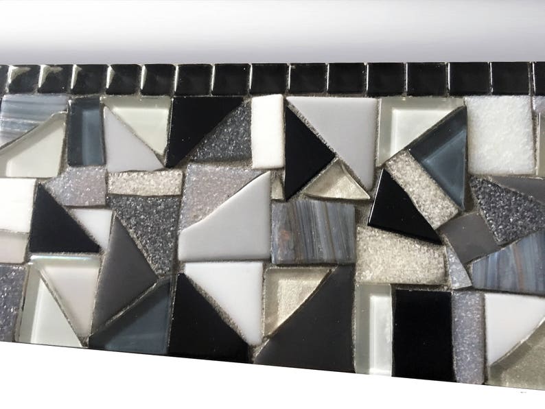 Puede incluir: Primer plano de un borde de mosaico hecho de peque&ntilde;os cuadrados y tri&aacute;ngulos negros, blancos y grises. Los azulejos de mosaico est&aacute;n dispuestos en un patr&oacute;n geom&eacute;trico.