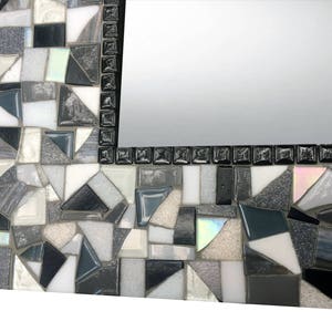 Puede incluir: Un marco de espejo de mosaico blanco y negro con un patr&oacute;n geom&eacute;trico. El marco est&aacute; hecho de peque&ntilde;as piezas irregulares de vidrio y azulejos.