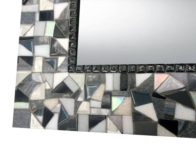 Puede incluir: Un marco de espejo de mosaico blanco y negro con un patr&oacute;n geom&eacute;trico. El marco est&aacute; hecho de peque&ntilde;as piezas irregulares de vidrio y azulejos.