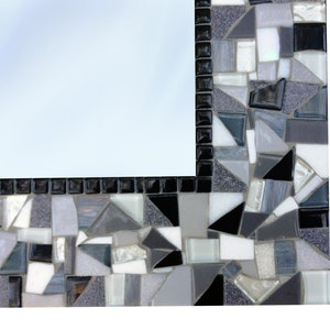 Puede incluir: Un marco de espejo de mosaico blanco y negro con una variedad de formas geom&eacute;tricas de diferentes tama&ntilde;os. El marco est&aacute; hecho de peque&ntilde;os trozos de vidrio y azulejos.