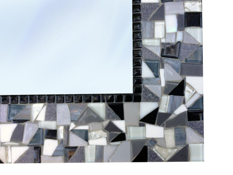 Puede incluir: Un marco de espejo de mosaico blanco y negro con una variedad de formas geom&eacute;tricas de diferentes tama&ntilde;os. El marco est&aacute; hecho de peque&ntilde;os trozos de vidrio y azulejos.