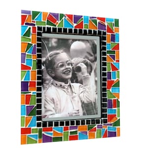 May include: A rectangular photo frame with a mosaic border. The mosaic is composed of colorful glass tiles in shades of red, orange, blue, green, and purple. The frame holds a black and white photograph of a person wearing glasses.