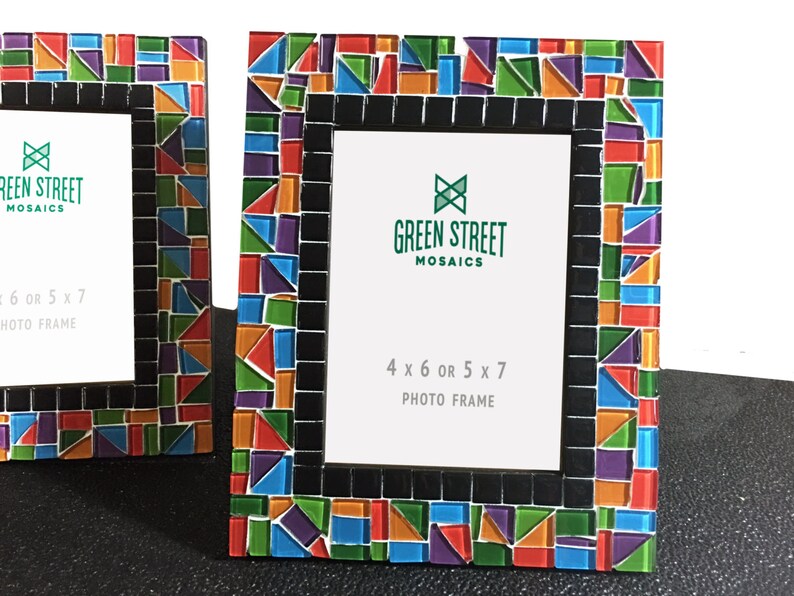 May include: Two photo frames with colorful mosaic tile borders. The frames have a black inner border and white space for photos. The text "GREEN STREET MOSAICS" and "4 x 6 OR 5 x 7 PHOTO FRAME" are visible on the frames.