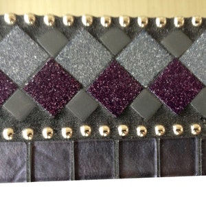 May include: A close-up of a decorative mosaic tile border with a checkerboard pattern of purple and gray glitter tiles. The border is accented with gold studs.