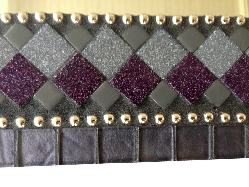 May include: A close-up of a decorative mosaic tile border with a checkerboard pattern of purple and gray glitter tiles. The border is accented with gold studs.