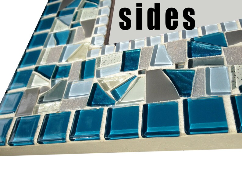 May include: Close-up of a mosaic mirror frame with blue, grey, and white tiles. The frame is made of small, irregular pieces of glass and has a rough, textured surface. The word "sides" is visible on the mirror.