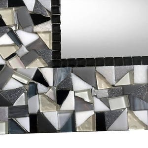 Puede incluir: Un marco de espejo de mosaico blanco y negro con un patr&oacute;n geom&eacute;trico. El marco est&aacute; hecho de peque&ntilde;as piezas irregulares de vidrio y azulejos.