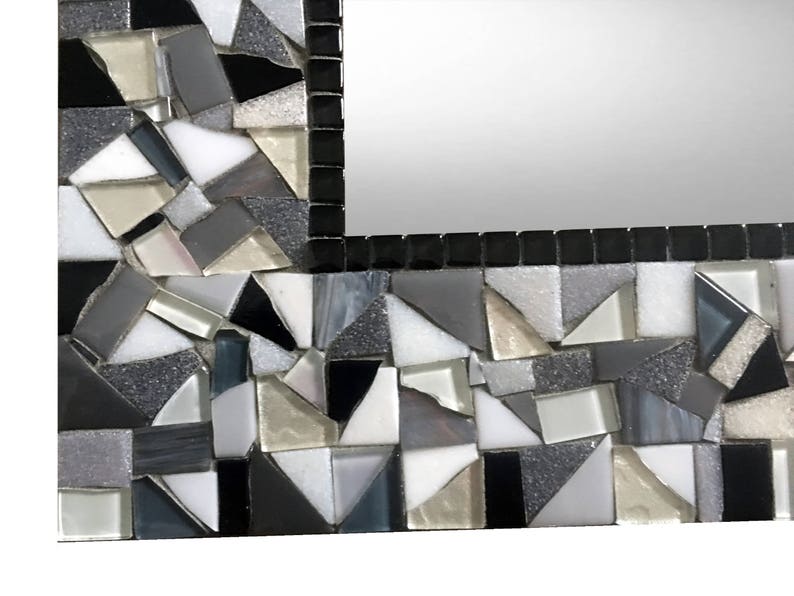 Puede incluir: Un marco de espejo de mosaico blanco y negro con un patr&oacute;n geom&eacute;trico. El marco est&aacute; hecho de peque&ntilde;as piezas irregulares de vidrio y azulejos.