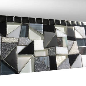 Puede incluir: Un borde de mosaico blanco y negro con un patr&oacute;n geom&eacute;trico. Los azulejos est&aacute;n dispuestos en un patr&oacute;n repetitivo de tri&aacute;ngulos y cuadrados.