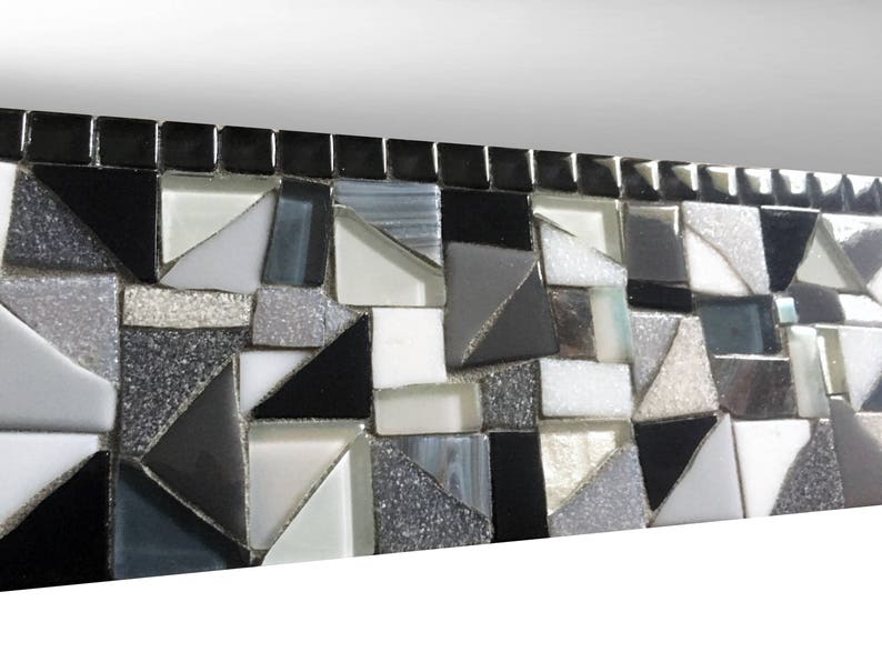 Puede incluir: Un borde de mosaico blanco y negro con un patr&oacute;n geom&eacute;trico. Los azulejos est&aacute;n dispuestos en un patr&oacute;n repetitivo de tri&aacute;ngulos y cuadrados.