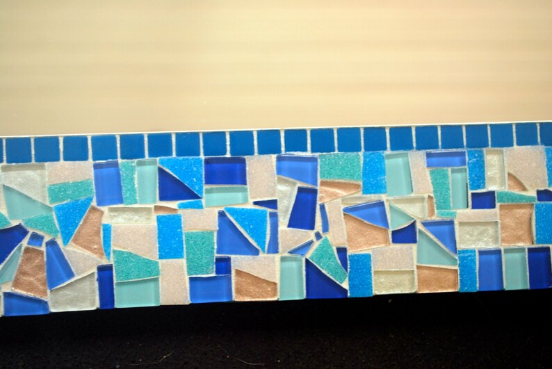 May include: A mosaic tile border featuring a mix of blue, white and light brown tiles. The tiles are arranged in a random pattern.