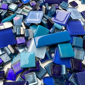 May include: A collection of blue and teal glass mosaic tiles in various sizes and shades. The tiles are arranged in a random pattern, creating a visually appealing and textured surface.