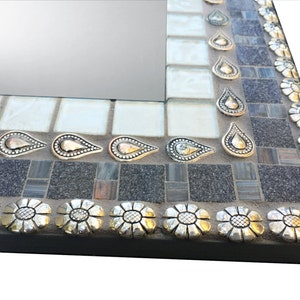 K&ouml;nnte beinhalten: Ein quadratischer Spiegel mit einem Mosaikrahmen. Der Rahmen besteht aus kleinen grauen, wei&szlig;en und braunen Fliesen. Der Rahmen ist mit silbernen und goldenen tropfenf&ouml;rmigen Akzenten und silbernen Blumenakzenten verziert.
