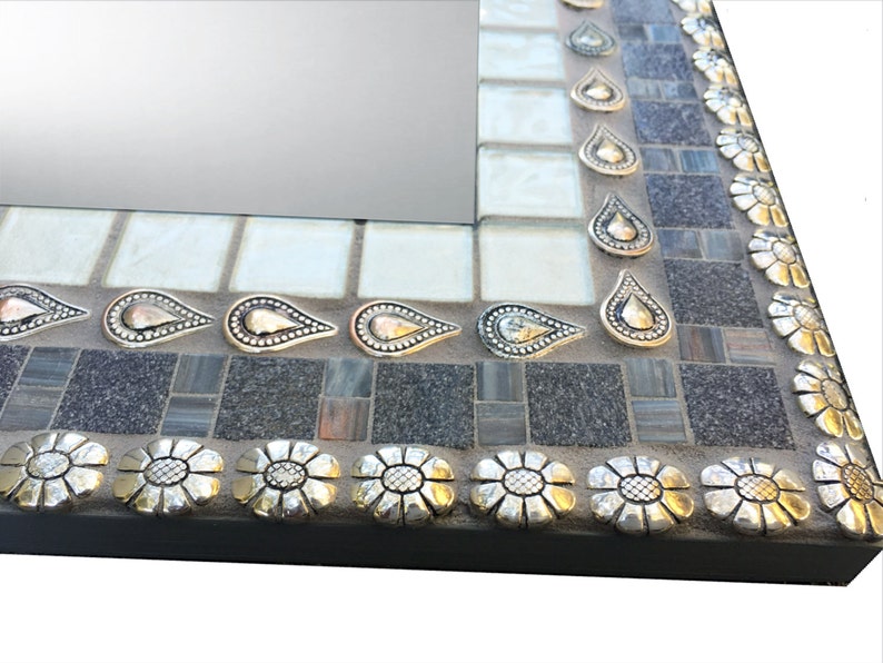 K&ouml;nnte beinhalten: Ein quadratischer Spiegel mit einem Mosaikrahmen. Der Rahmen besteht aus kleinen grauen, wei&szlig;en und braunen Fliesen. Der Rahmen ist mit silbernen und goldenen tropfenf&ouml;rmigen Akzenten und silbernen Blumenakzenten verziert.