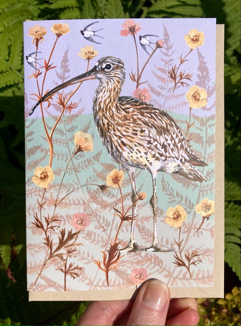 May include: A greeting card featuring a brown and white bird with a long beak standing in a field of yellow and pink flowers. The background is a light blue color.