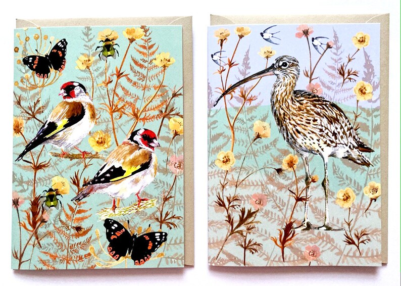 May include: Two greeting cards with nature-themed illustrations. The first card features two goldfinches perched on branches with a butterfly and a beetle. The second card features a long-billed curlew standing in a field of flowers.