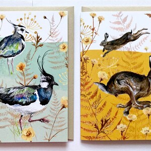 May include: Two greeting cards with nature-themed illustrations. The card on the left features a pair of lapwings in a green and brown floral pattern. The card on the right features a pair of hares in a yellow and brown floral pattern.