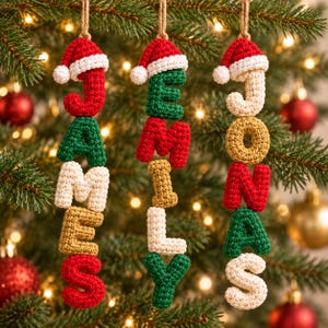 May include: Three vertical hanging ornaments made of crocheted letters spelling the names James, Jemily, and Jonas. Each ornament is topped with a small red and white crocheted Santa hat and hangs from a tan twine loop against a pine tree.