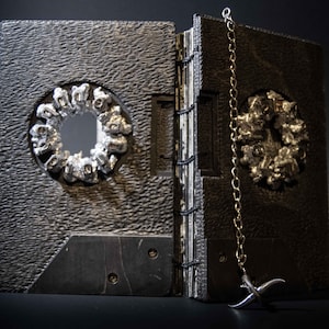 May include: A black leather-bound journal with a silver chain and a silver ornament on the front cover. The ornament is a circle with a hole in the centre and is made of many small silver pieces.