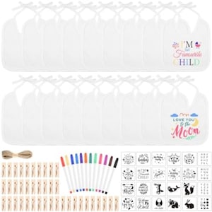 Op de afbeelding: Een set witte slabbetjes met striksluiting, waaronder één bedrukt met "I'M THE FAVOURITE CHILD" en één met "LOVE YOU TO THE MOON". De set bevat kleurrijke stiften, houten wasknijpers, touw en een vel met diverse grafische stickers voor decoratie.