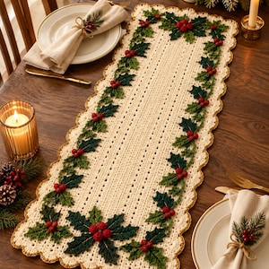 May include: A rectangular cream-colored crochet table runner featuring a scalloped edge with a gold trim. The runner is decorated with a repeating pattern of dark green crocheted holly leaves and clusters of small red berries along the border.