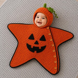May include: A star-shaped orange crochet baby bunting with a jack-o'-lantern face featuring black eyes, a nose, and a mouth. The garment includes an attached hood with a green stem and leaf, and a side closure with eight light brown buttons.