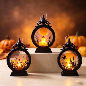 May include: Three black circular lanterns with metal handles, each featuring an illuminated orange moon and intricate Halloween-themed silhouettes including haunted houses, bare trees, flying bats, and a witch on a broomstick against a warm glow.