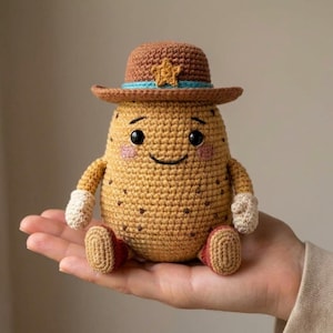 Op de afbeelding: Een gehaakte aardappelpop met een bruine cowboyhoed met een blauwe band en een gele sterbadge. De pop heeft een beige lichaam met donkerbruine vlekken, zwarte kraaloogjes, een geborduurde glimlach, roze wangen, witte wanten en rode laarzen.