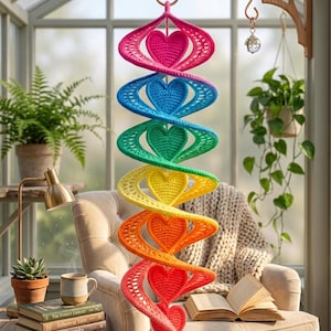 May include: A hanging spiral wind spinner crafted from crocheted yarn in a vibrant rainbow gradient. The structure features a series of six interconnected heart-shaped motifs, each matching the colour of its corresponding spiral section in pink, blue, green, yellow, orange, and red.