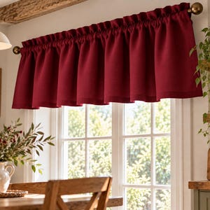 May include: A deep red window valance featuring a rod pocket header with a ruffled top edge. The fabric is opaque and hangs in uniform vertical folds across a brass-toned curtain rod, providing a solid color accent for a window treatment.