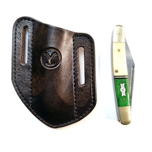 May include: A black leather knife sheath with a stamped logo and a pocket knife. The knife has a cream-colored handle with green accents and a silver blade. The knife is closed.