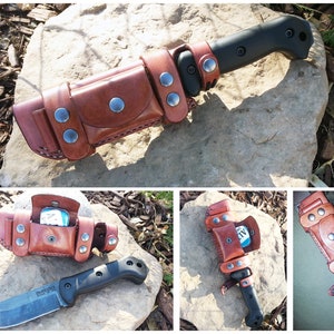 May include: A black survival knife with a brown leather sheath. The sheath has multiple compartments and is secured with silver-colored rivets. The knife is resting on a large rock, with a natural background.