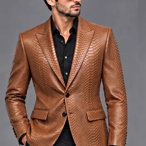 May include: A tan blazer with a textured snakeskin pattern, featuring a notched lapel, two black front buttons, and two flap pockets. The blazer is worn over a black button-down shirt, paired with black trousers and black sunglasses.