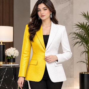 Op de afbeelding: Een tweekleurige blazer met een felgele rechterkant en een helderwitte linkerkant, beide voorzien van een gestructureerd slangenleerpatroon. Het kledingstuk heeft een reverskraag, een enkele knoopsluiting aan de voorzijde en twee klepzakken.