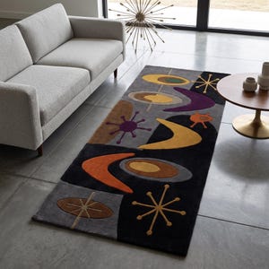 May include: A rectangular area rug featuring a dark grey and black background with a repeating pattern of abstract shapes including yellow, orange, purple, and brown boomerangs, circles, and starbursts in a tufted texture across the entire surface.