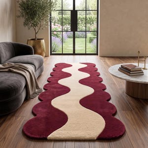May include: A long, rectangular runner rug featuring a wavy, scalloped edge design. The rug displays a bold, deep burgundy colour on the sides with a wide, flowing cream-coloured wave pattern running through the centre, creating a distinct contrast.