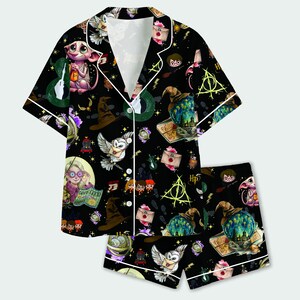 May include: A black short-sleeved button-down pajama shirt and matching shorts set featuring a colorful all-over print of Harry Potter characters, owls, letters, sorting hats, and magical symbols with white piping along the edges and collar.