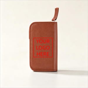 May include: A rectangular brown leather key case with rounded corners and a zipper closure. The front surface features a red square outline containing the text YOUR LOGO HERE in red capital letters. A small leather pull tab is attached to the zipper.