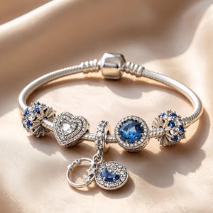 Può includere: Un bracciale con ciondoli in argento caratterizzato da un cuore centrale con pietre chiare, un ciondolo rotondo con una pietra blu, due elementi sferici con pietre blu e chiare e un ciondolo pendente a forma di mezzaluna e stelle.