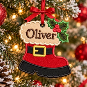 May include: A red and black felt Christmas boot ornament featuring a white scalloped cuff embroidered with the name Oliver in brown thread. The boot has a black belt with a yellow buckle and a green holly leaf accent with red berries.