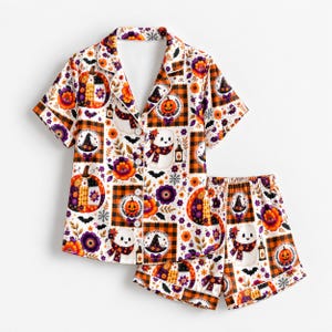 May include: A short-sleeve button-down pajama shirt and matching shorts set featuring a white background with a repeating pattern of orange pumpkins, purple flowers, black bats, witch hats, lanterns, and orange and black plaid squares.
