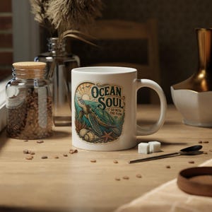 May include: A white ceramic mug featuring a colorful graphic of a sea turtle swimming near coral and seashells. The text "OCEAN SOUL" and "GO WITH THE FLOW" is printed above the turtle, with a sun rising over the horizon in the background.