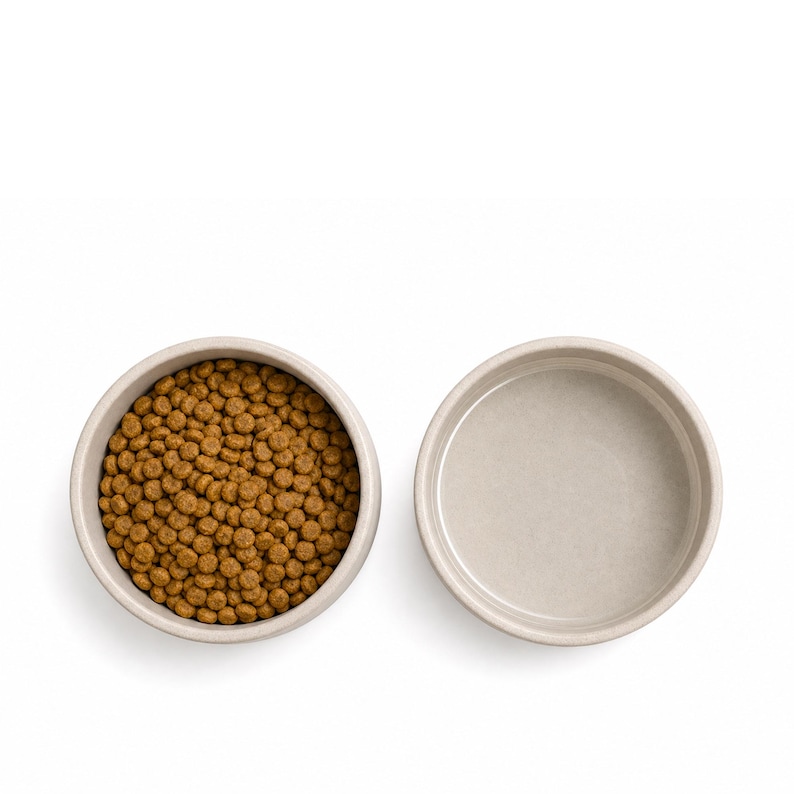 Top view of two stoneware ceramic pet bowls in oatmeal, one filled with dry food and one empty, showing the fully glazed matte interior