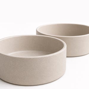 Close view of two oatmeal speckled stoneware pet bowls showing the matte glaze, fine dark iron speckle and thick straight-sided wall of the MOTO ceramic bowl