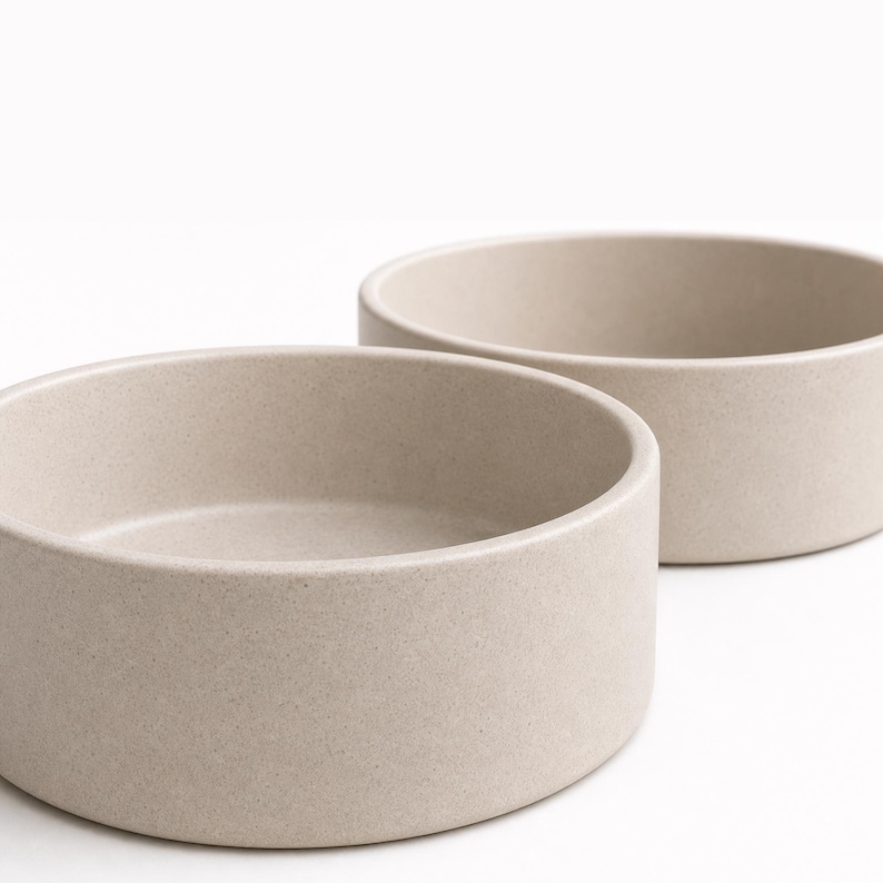 Close view of two oatmeal speckled stoneware pet bowls showing the matte glaze, fine dark iron speckle and thick straight-sided wall of the MOTO ceramic bowl