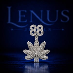 May include: A silver-toned pendant featuring the number 88 positioned above a leaf-shaped design. The entire surface of the pendant is covered in small, clear, sparkling stones that create a reflective, textured appearance against the dark background.