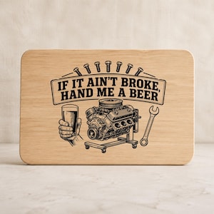 May include: A rectangular light-colored wooden cutting board featuring a black laser-engraved graphic of a car engine, a hand holding a beer glass, and a wrench. The text reads, "IF IT AIN'T BROKE, HAND ME A BEER," with a row of bolts above.