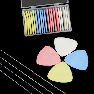 May include: A set of triangular tailor's chalk pieces in yellow, blue, pink, and white, stored in a clear plastic rectangular container. Four individual pieces are arranged in a cluster below the container, with thin white chalk lines drawn diagonally.