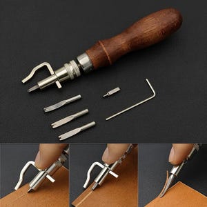 May include: A leathercraft groover and creaser tool featuring a dark brown wooden handle, a silver metal adjustable head, and several interchangeable metal tips. The set includes a small L-shaped hex key for tightening the various attachments.